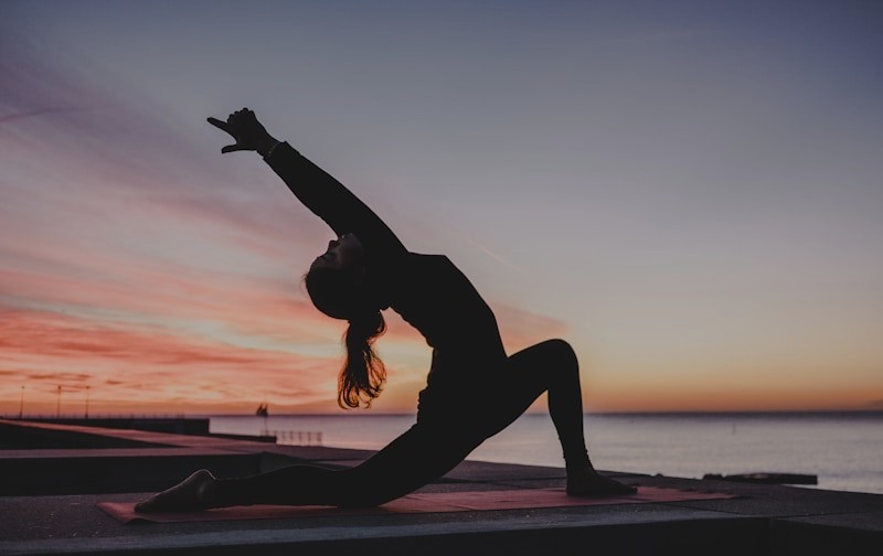 Silhouette of a person in a yoga pose on a pier at sunset